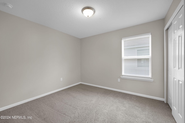 unfurnished bedroom with a textured ceiling, carpet, and a closet