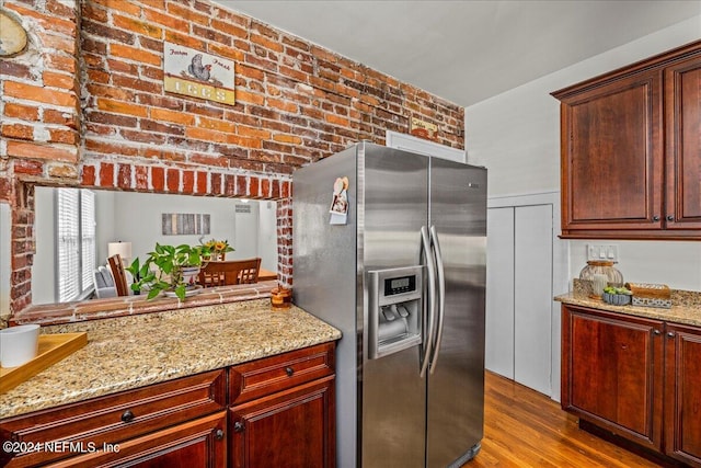 kitchen featuring light stone counters, stainless steel fridge with ice dispenser, brick wall, and light wood-type flooring