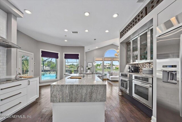 kitchen featuring dark hardwood / wood-style flooring, stainless steel appliances, a kitchen island with sink, wall chimney range hood, and white cabinets