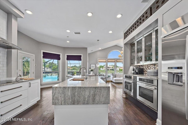 kitchen featuring white cabinets, an island with sink, wall chimney exhaust hood, glass insert cabinets, and stainless steel appliances