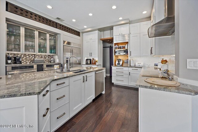 kitchen featuring wall chimney exhaust hood, dark hardwood / wood-style floors, decorative backsplash, appliances with stainless steel finishes, and white cabinetry