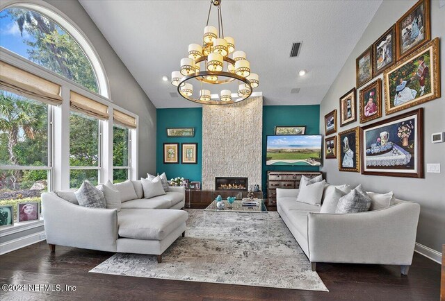 living room featuring lofted ceiling, an inviting chandelier, a textured ceiling, a fireplace, and dark hardwood / wood-style flooring