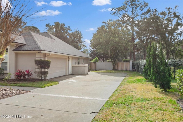 view of property exterior featuring a garage, fence, concrete driveway, a lawn, and stucco siding