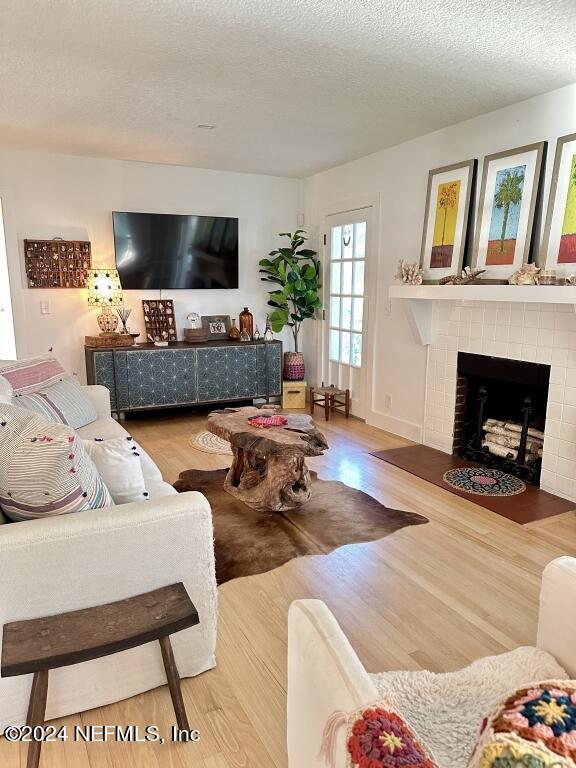 living room with a textured ceiling, light wood-type flooring, and a tile fireplace