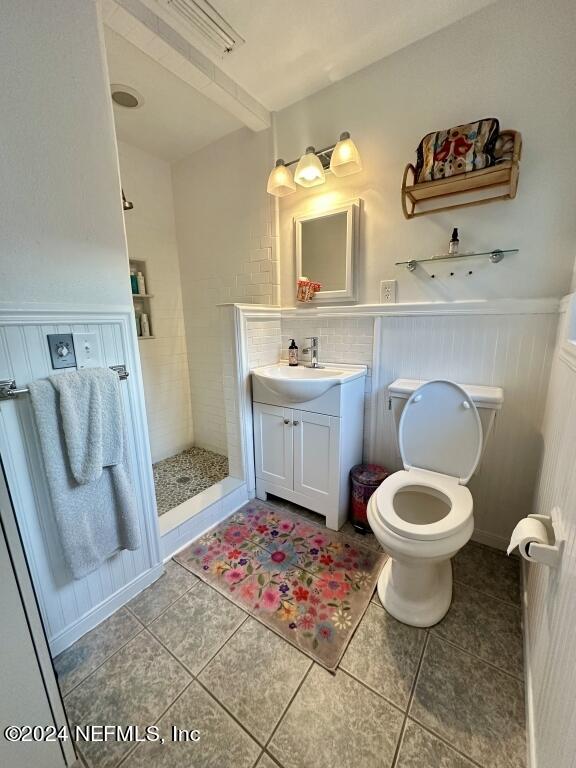 bathroom featuring tiled shower, tasteful backsplash, tile patterned flooring, vanity, and toilet