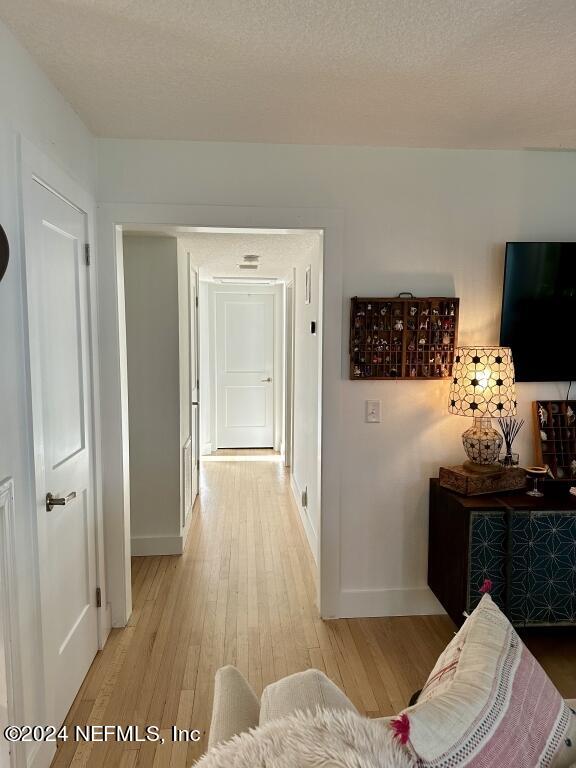 hallway with light wood-type flooring and a textured ceiling