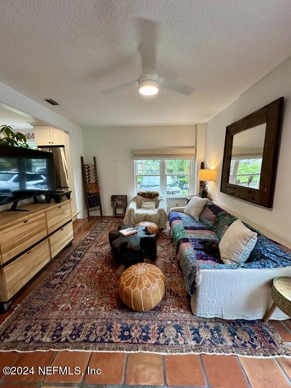 tiled living room with ceiling fan and a textured ceiling