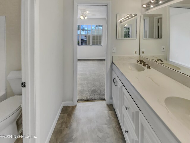 bathroom featuring ceiling fan, toilet, double sink vanity, and tile patterned floors