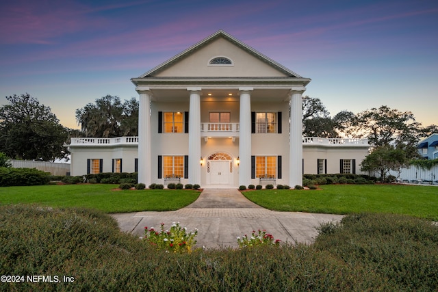 greek revival house with stucco siding, a balcony, and a yard