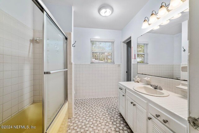 bathroom featuring tile walls, combined bath / shower with glass door, and vanity