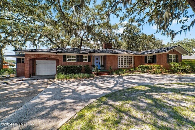 single story home featuring an attached garage, brick siding, driveway, and a chimney