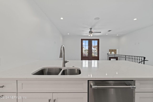 kitchen with stainless steel dishwasher, sink, white cabinetry, ceiling fan, and light stone counters