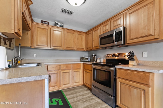 kitchen featuring sink, light wood-type flooring, a textured ceiling, and stainless steel appliances