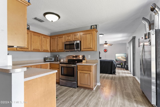 kitchen with light hardwood / wood-style floors, a textured ceiling, ceiling fan, stainless steel appliances, and kitchen peninsula