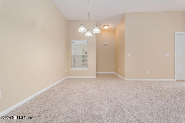 spare room with carpet floors, an inviting chandelier, and baseboards