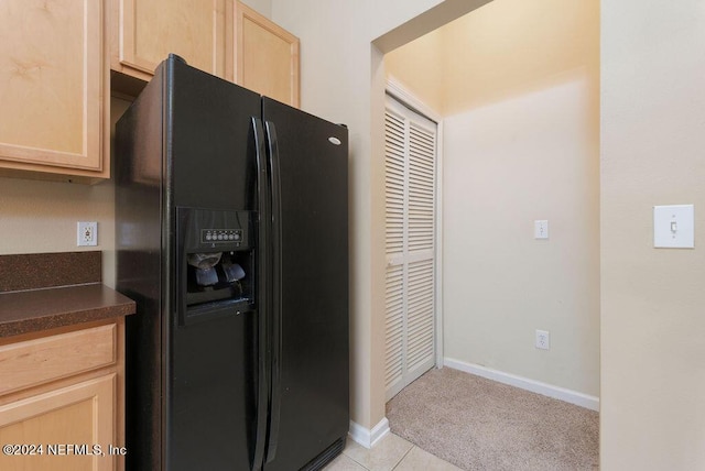 kitchen featuring dark countertops, light brown cabinetry, baseboards, and black fridge