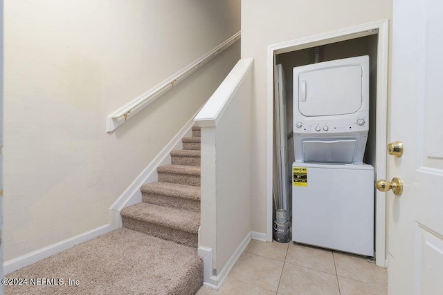 clothes washing area with laundry area, baseboards, light tile patterned flooring, and stacked washer and clothes dryer