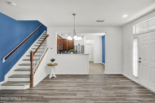 foyer entrance with a textured ceiling, hardwood / wood-style floors, and an inviting chandelier