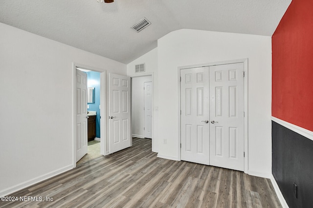 unfurnished bedroom with hardwood / wood-style floors, a closet, a textured ceiling, and lofted ceiling