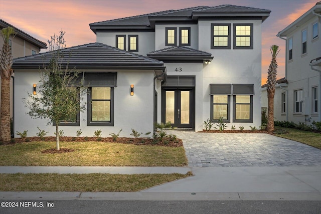 prairie-style house with french doors, a tile roof, a lawn, and stucco siding