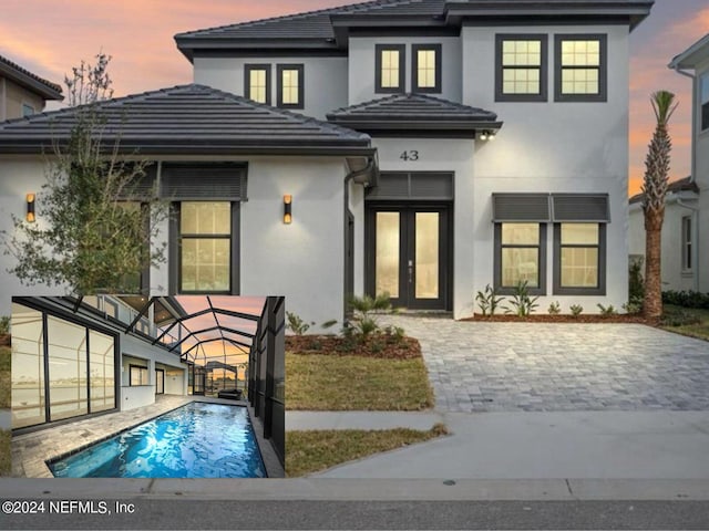 back of property at dusk with a lanai, a tile roof, an outdoor pool, and stucco siding