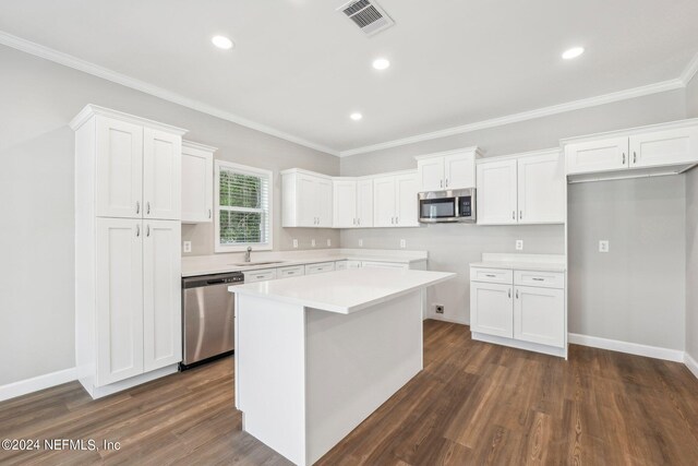 kitchen with ornamental molding, stainless steel appliances, dark wood finished floors, a kitchen island, and white cabinets
