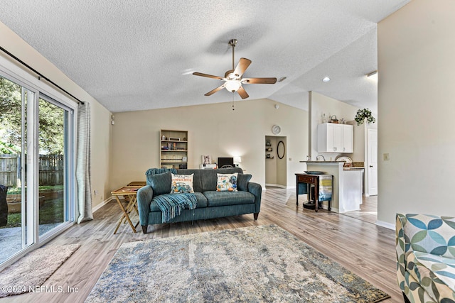 living room with ceiling fan, light wood-type flooring, a fireplace, a textured ceiling, and lofted ceiling