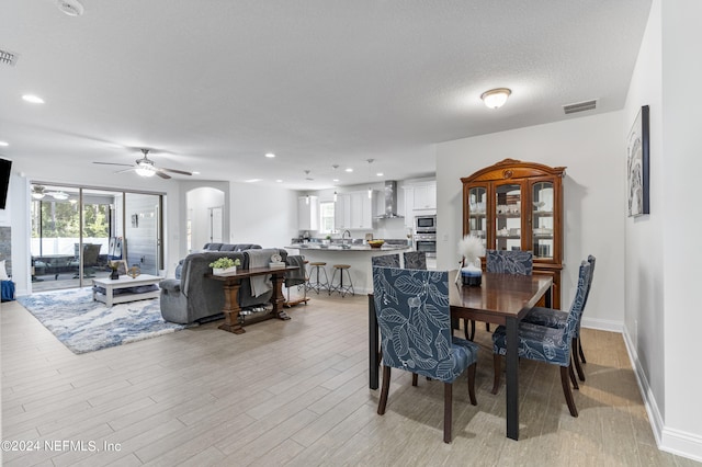 dining space featuring a textured ceiling, arched walkways, visible vents, and light wood-style floors