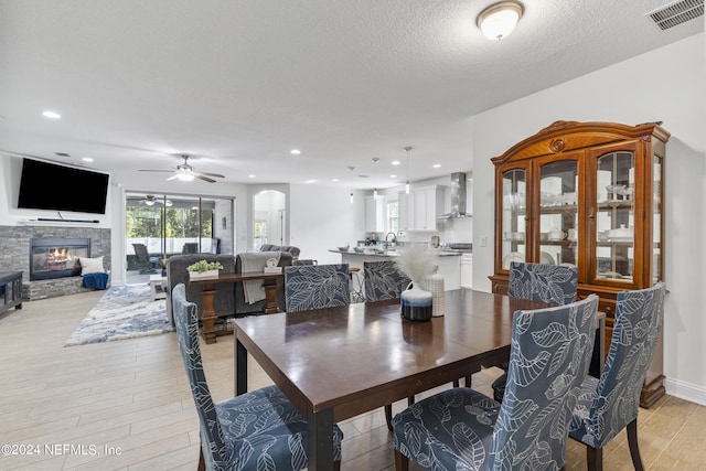 dining area featuring recessed lighting, visible vents, light wood-style floors, a stone fireplace, and a textured ceiling