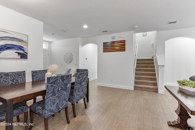 dining room featuring arched walkways, visible vents, light wood-style floors, a textured ceiling, and stairs