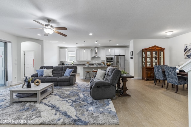 living room with arched walkways, light wood finished floors, a textured ceiling, and recessed lighting