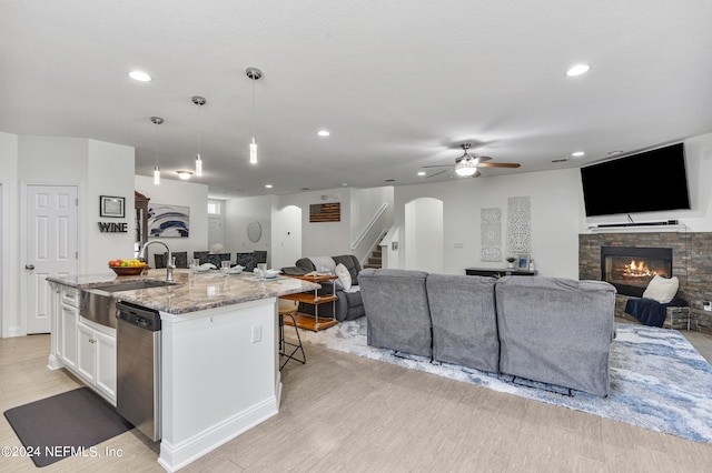 kitchen featuring white cabinetry, open floor plan, hanging light fixtures, stainless steel dishwasher, and a center island with sink