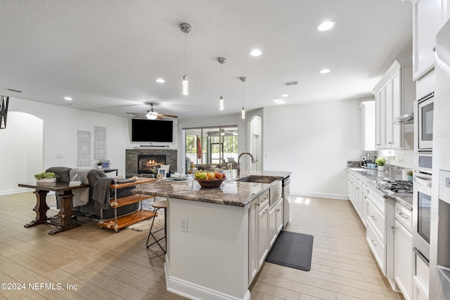 kitchen with stone countertops, white cabinetry, hanging light fixtures, and an island with sink