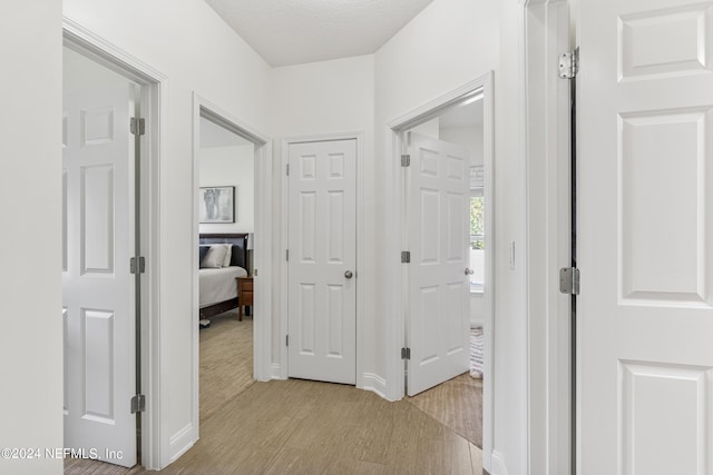 corridor with a textured ceiling and light wood-style flooring