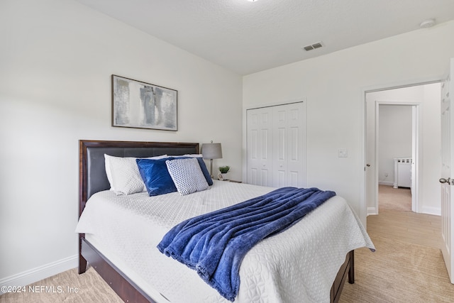 bedroom with a textured ceiling, visible vents, baseboards, a closet, and light wood finished floors