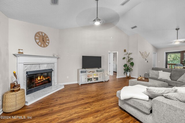 living room featuring ceiling fan, high vaulted ceiling, hardwood / wood-style floors, a fireplace, and a textured ceiling