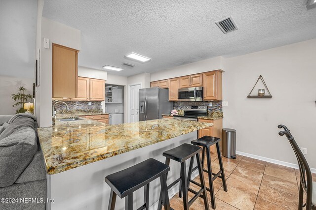 kitchen featuring stainless steel appliances, decorative backsplash, light stone counters, a textured ceiling, and light tile patterned flooring