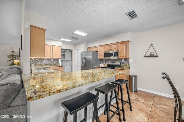 kitchen featuring a peninsula, visible vents, stainless steel appliances, and light stone counters