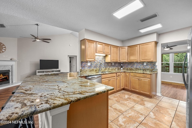 kitchen with visible vents, dishwasher, a premium fireplace, light stone countertops, and a sink