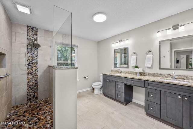 bathroom with tile patterned flooring, a textured ceiling, a tile shower, toilet, and dual vanity