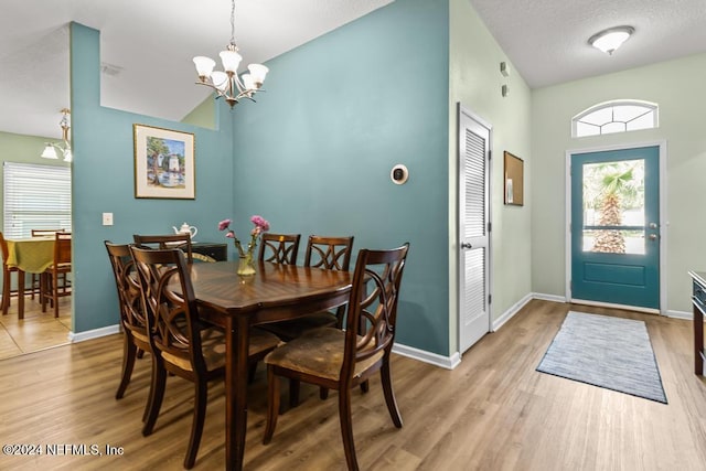 dining room featuring lofted ceiling, wood-type flooring, a textured ceiling, and an inviting chandelier