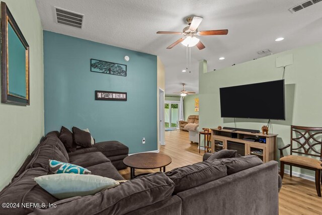 living room featuring light wood-type flooring, ceiling fan, and a textured ceiling