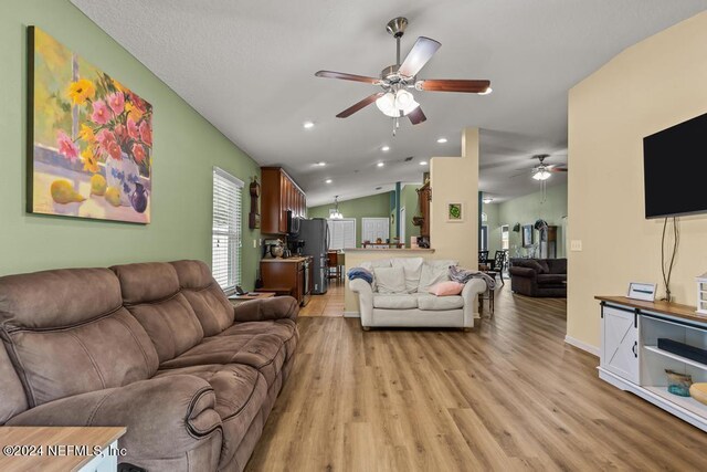 living room with ceiling fan, vaulted ceiling, and light hardwood / wood-style floors