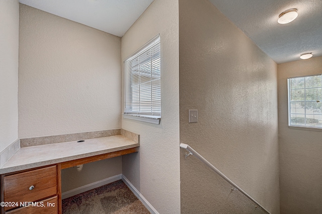 unfurnished office featuring a textured ceiling, dark colored carpet, and built in desk