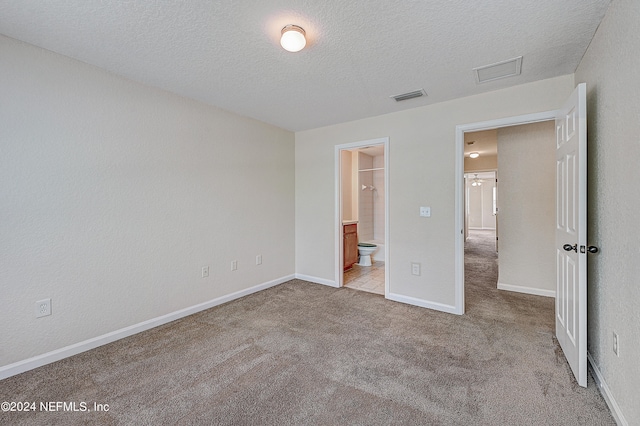 unfurnished bedroom featuring light colored carpet, a textured ceiling, and ensuite bath