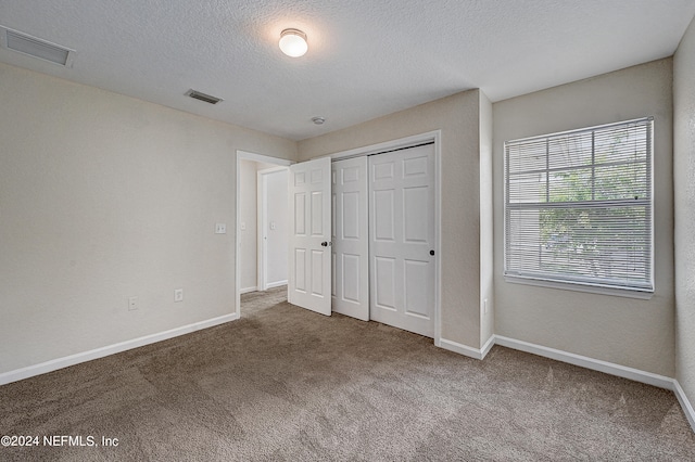 unfurnished bedroom featuring a textured ceiling, carpet floors, and a closet