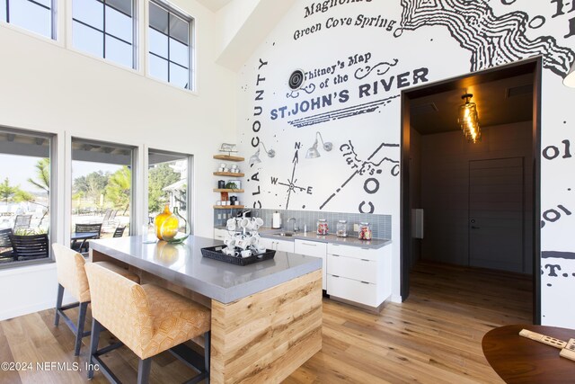 kitchen with sink, decorative backsplash, light wood-type flooring, a towering ceiling, and white cabinetry