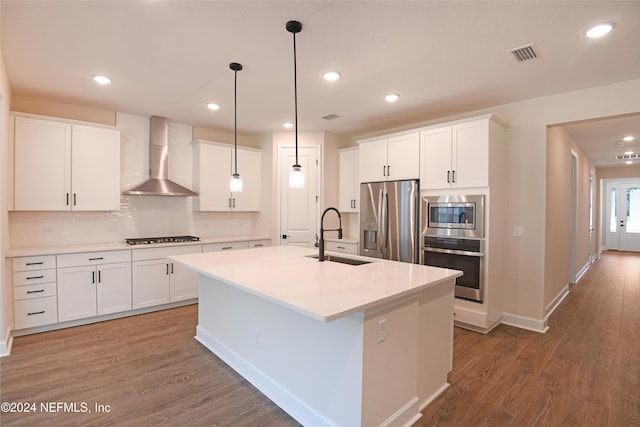 kitchen featuring white cabinetry, sink, wall chimney exhaust hood, stainless steel appliances, and a kitchen island with sink