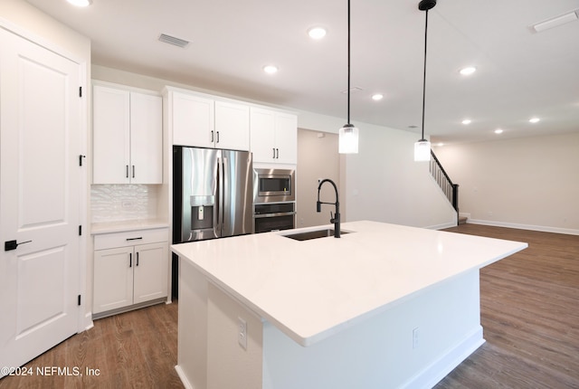 kitchen featuring white cabinetry, sink, hanging light fixtures, stainless steel appliances, and a center island with sink