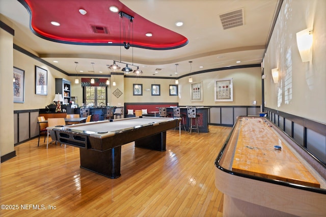 rec room with a tray ceiling, light wood-type flooring, ornamental molding, and bar area